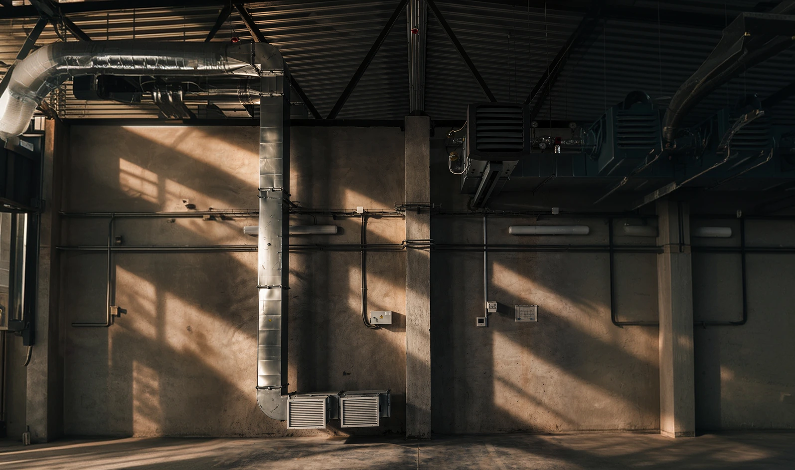 Intérieur de style industriel avec des conduits métalliques et des jeux d'ombre et de lumière naturelle.