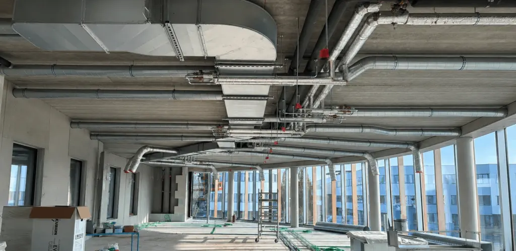 Espace de bureau en construction avec conduits au plafond pour le projet Semlex à Drogenbos.